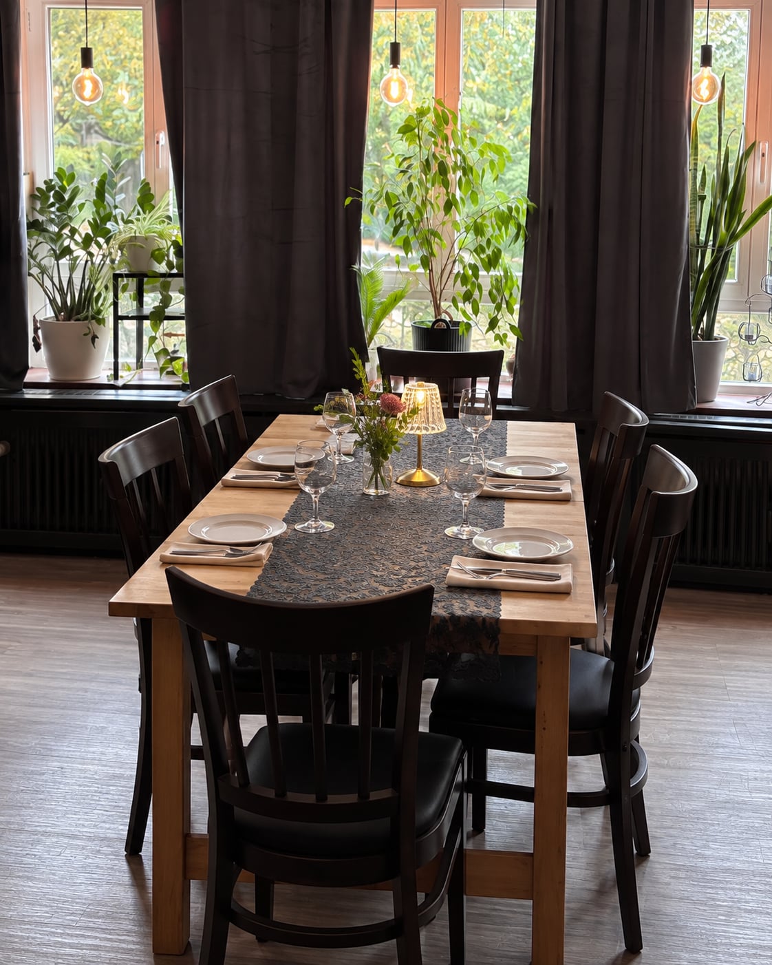 Gedeckter Holztisch mit Gläsern, Servietten, Blumen und Tischleuchte