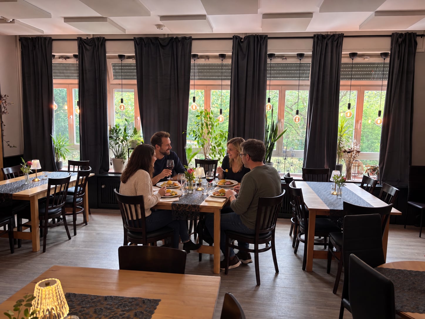 Vier Gäste essen und unterhalten sich an einem Tisch am Fenster