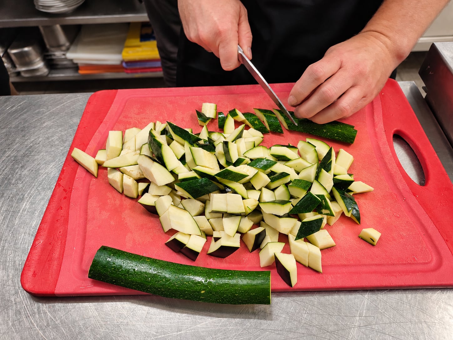 Hände schneiden Zucchini auf einem roten Brett